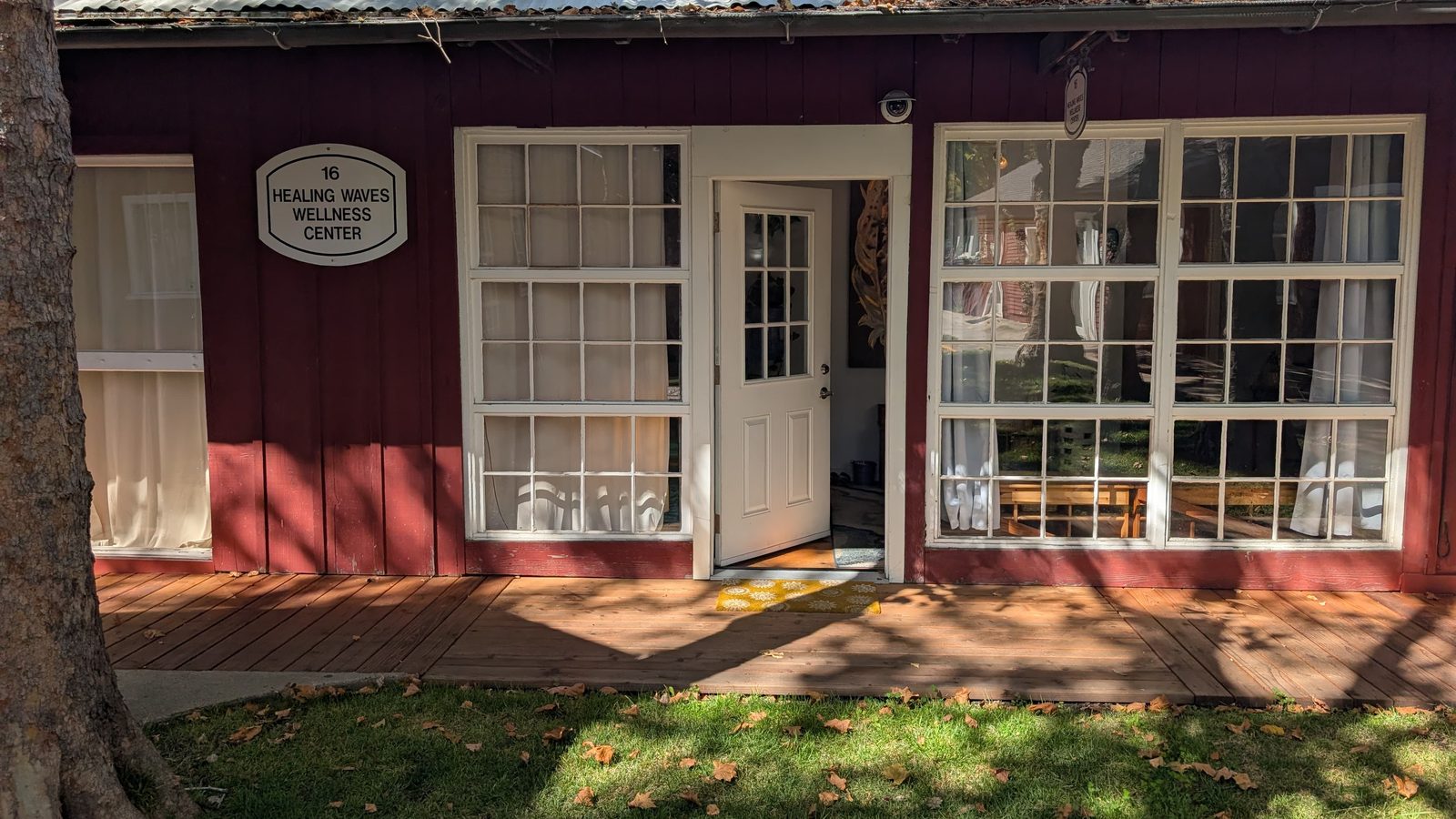 The front door of Healing Waves Wellness Center, a red wood building with white trim and a wide deck under a tree